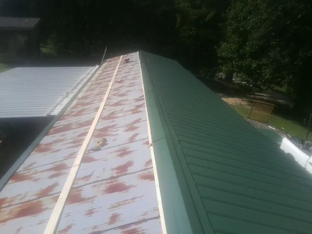 Old rusted panels beside newly installed green metal roofing — Wind Damage Roof Repair by Roofing Brothers in Monroe