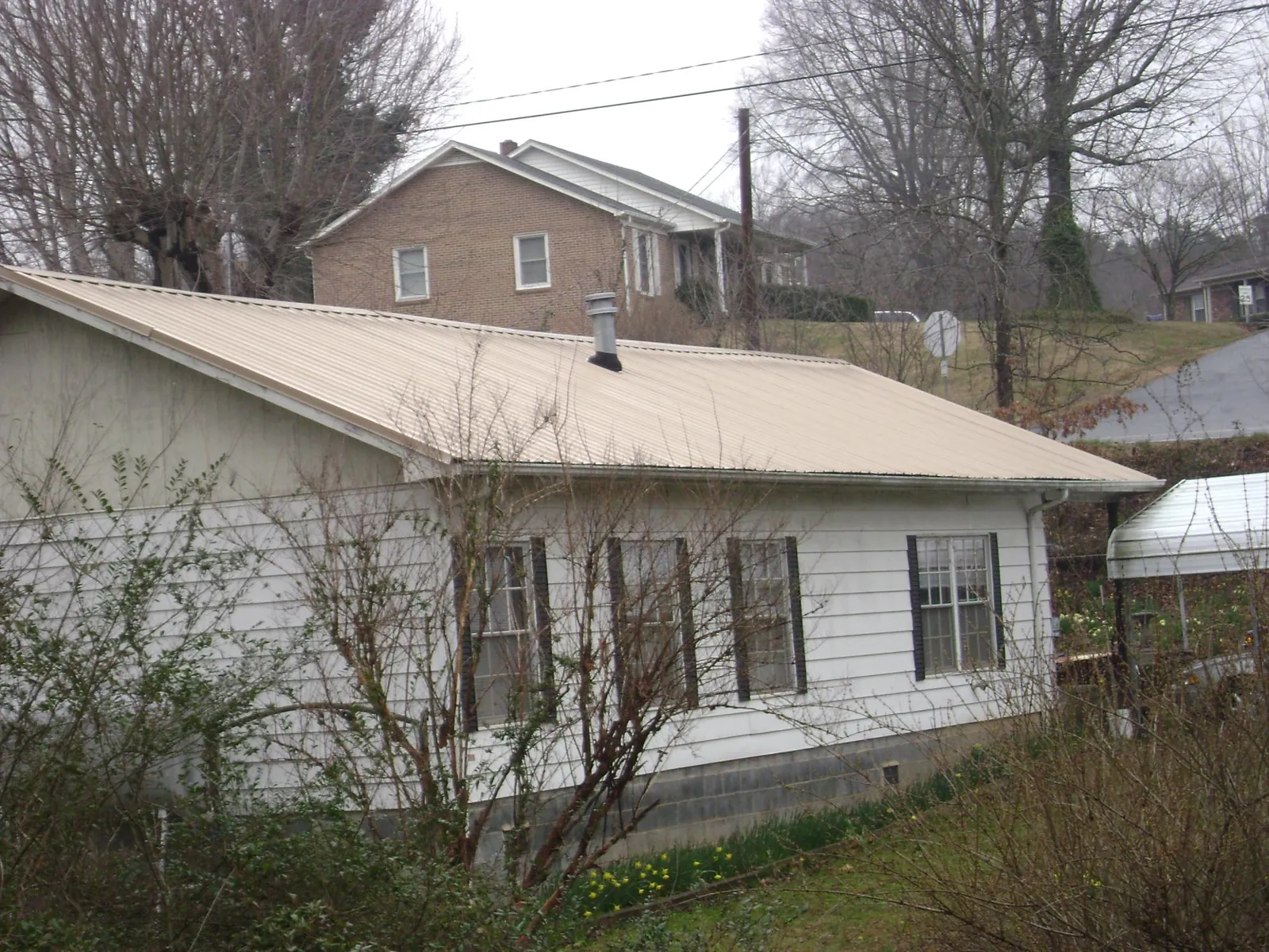 Tan metal roof on a white sided house set into a hillside — Commercial Roofing by Roofing Brothers in Monroe